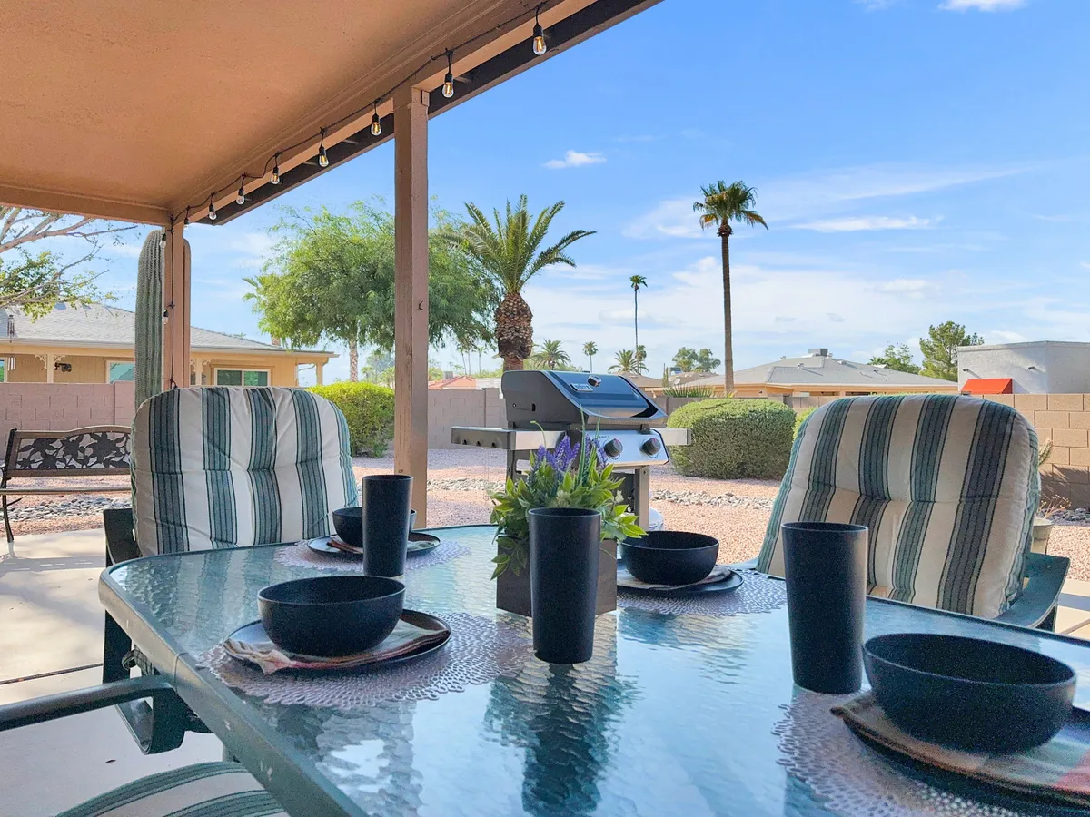 This image captures a charming patio area with a table set for dining and a charcoal grill, all nestled under the shade of palm trees. The setup suggests both casual sunset barbecues and comfortable daytime lounging, with the landscape adding to the tranquil experience.