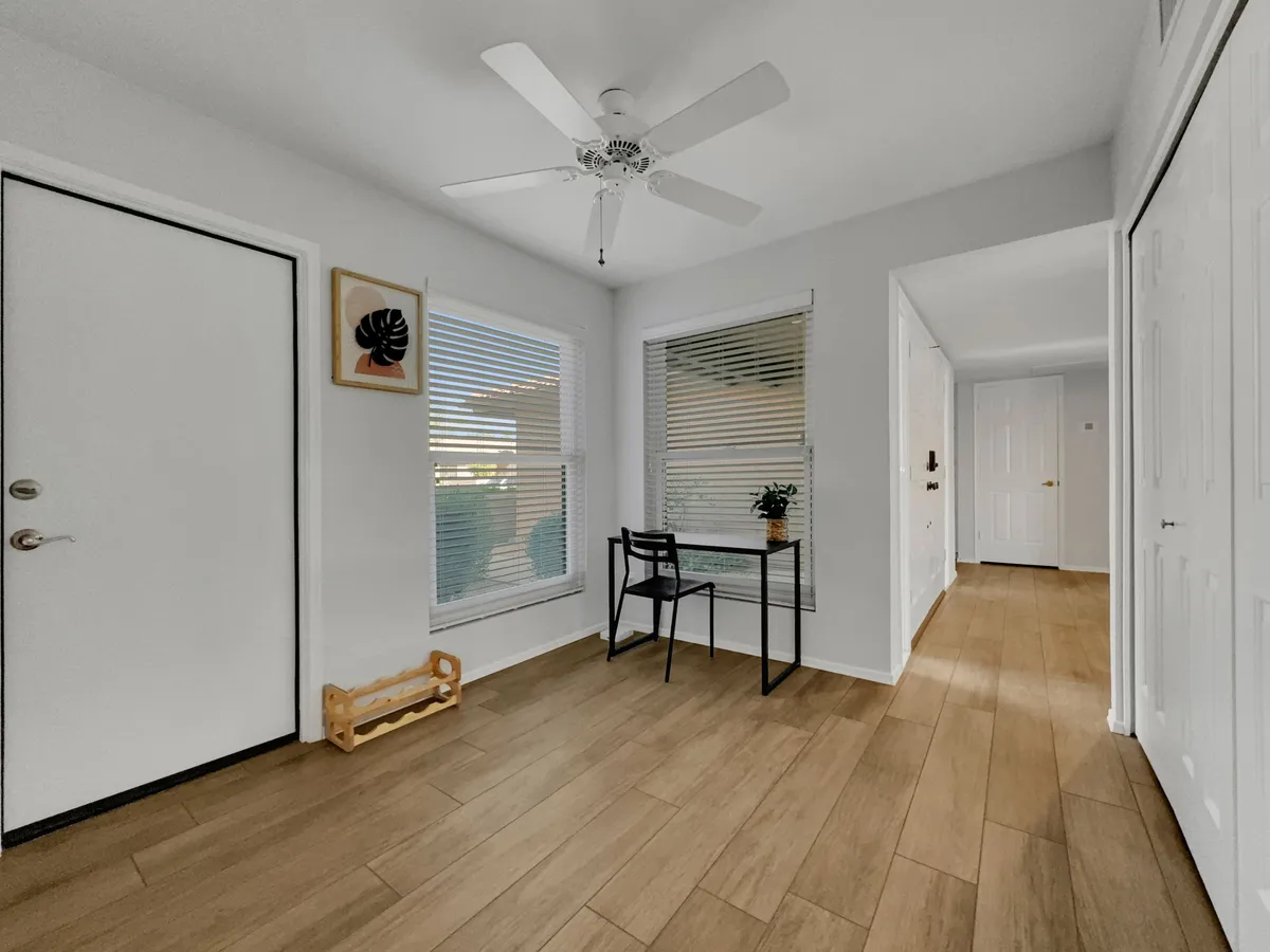 A welcoming entryway with a front door, a work desk and chair, a decorative plant, and framed artwork. The space is bright and inviting, illustrating the comforts of home and an ideal remote work setup for long-term guests.