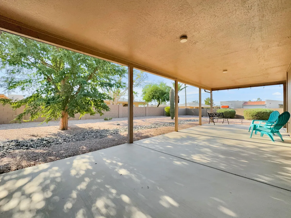 An outdoor seating area with green chairs and a table set under mature trees, in a beautifully landscaped yard. The tranquil scene suggests a perfect spot for relaxing after a round of golf or enjoying social hours with friends and neighbors.