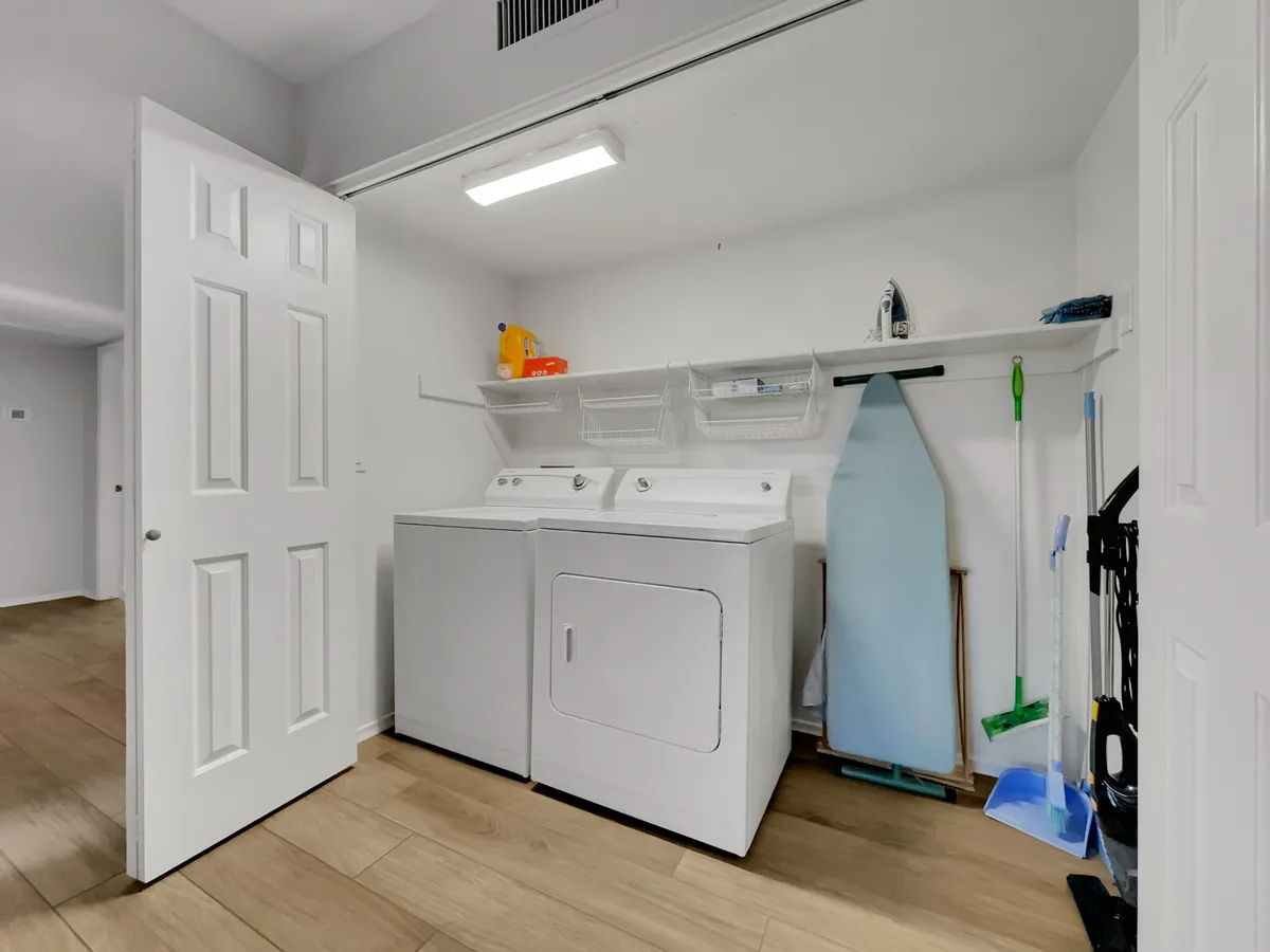 A well-organized laundry room with a washing machine, dryer, ironing board, and cleaning supplies. The layout is practical and tidy, supporting efficient daily routines.