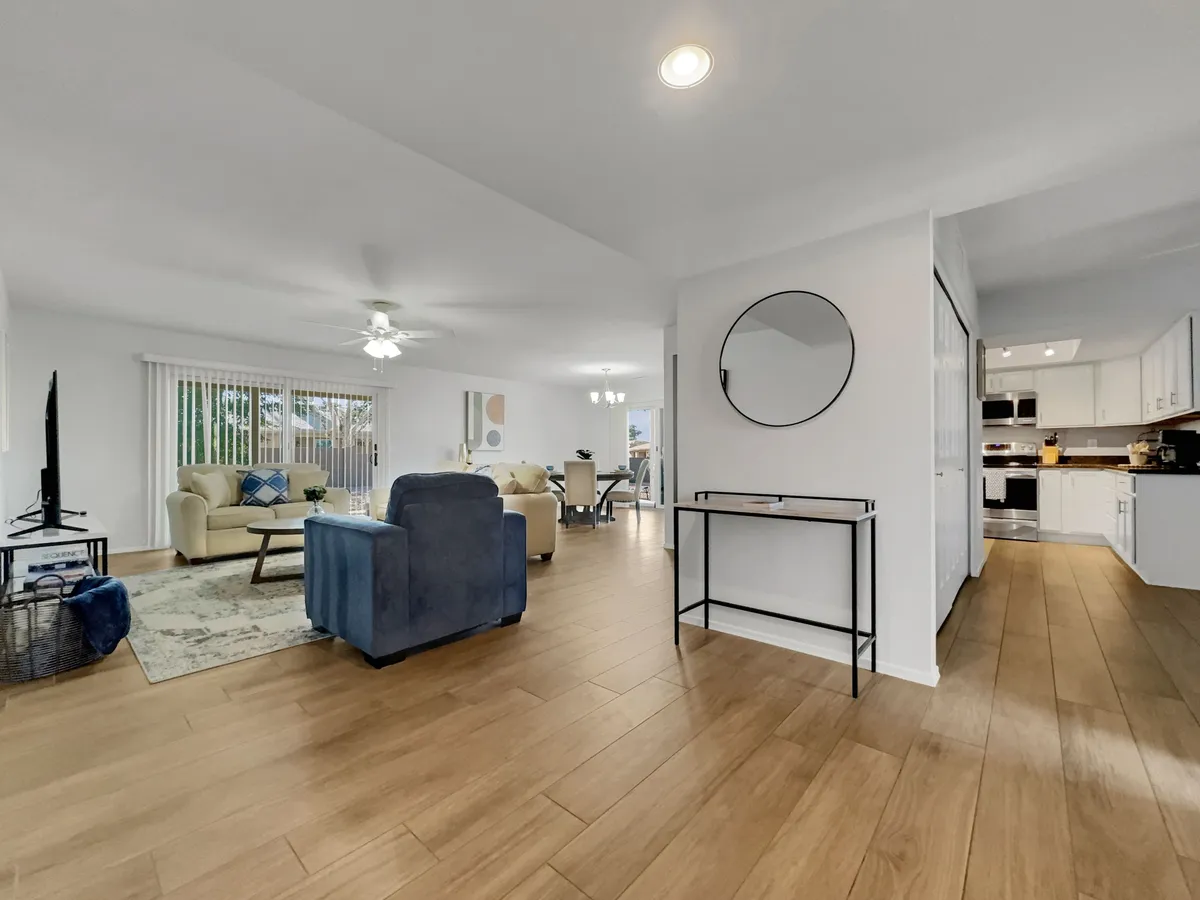 An open-plan view featuring a light-colored sofa and blue armchair facing a stylish dining table, all set against contemporary decor. A mirror on the wall and modern finishes enhance the sense of space and recent remodeling.