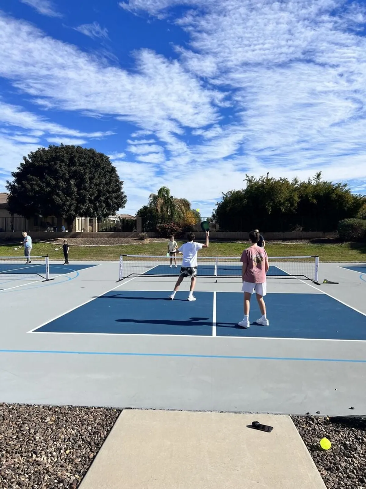 This image features an exterior tennis court with players actively engaged in a match. The clear sky and the inviting, well-maintained court set the scene for friendly competition and outdoor socializing—core aspects of country club life.