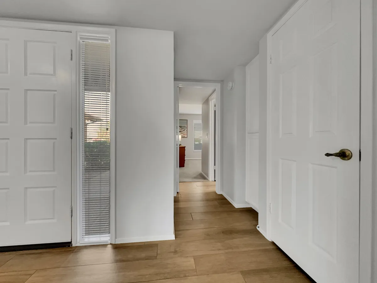 A welcoming entryway with a front door opening onto light wood flooring and a spacious hallway. The space feels inviting and airy, offering a glimpse of the home's interior and suggesting a warm welcome for arriving guests or family members.