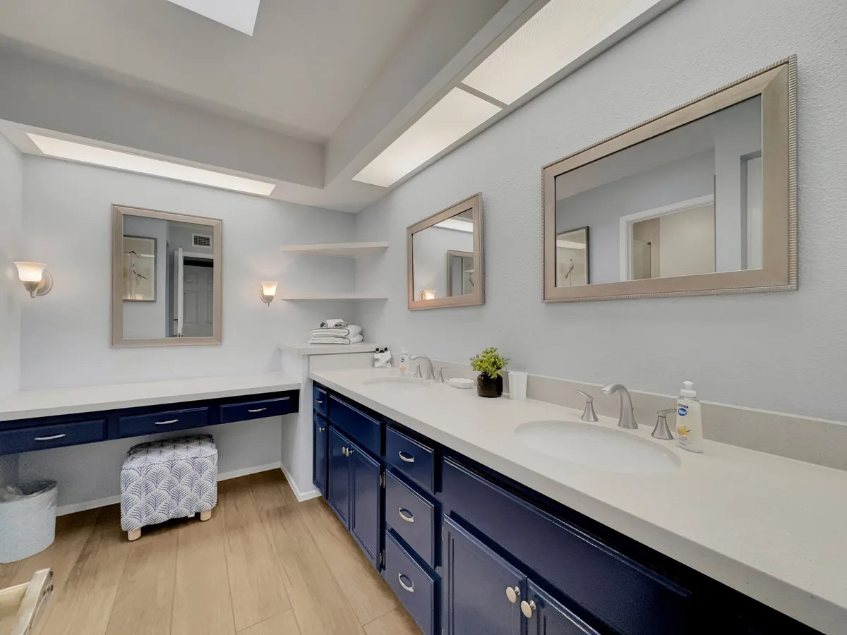 A modern en-suite bathroom featuring dual sinks, large mirrors, a spacious vanity area, and neatly organized towel storage. The inviting and tranquil design suggests ample space for personal grooming and relaxation.
